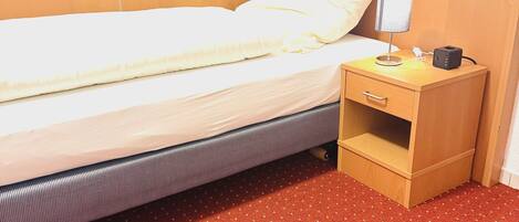 A bed with a wooden headboard, a bedside table with a lamp, and a red patterned carpet.