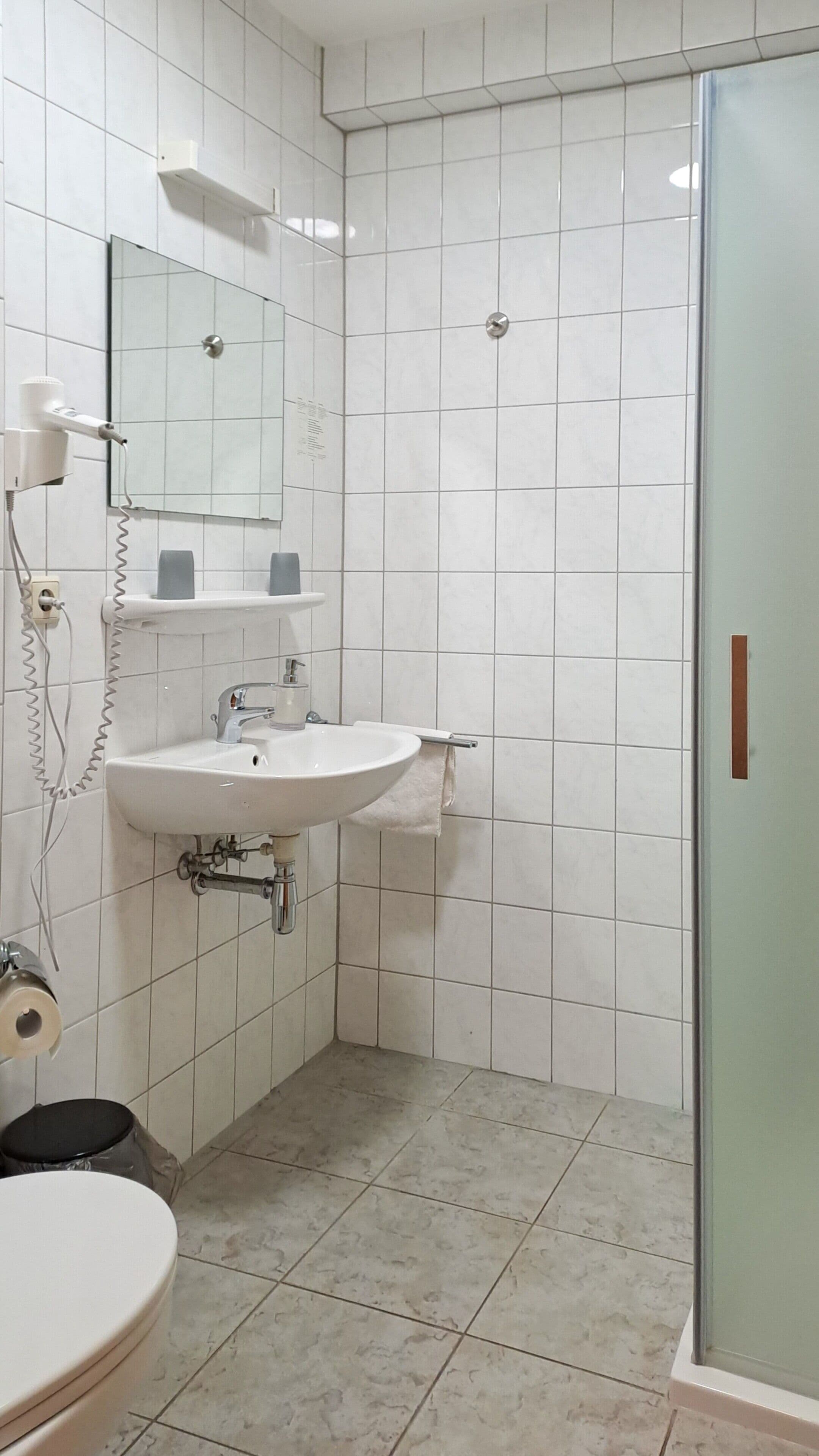 Une salle de bain équipée d’un lavabo, d’un miroir, d’un porte-serviettes et d’un espace douche.