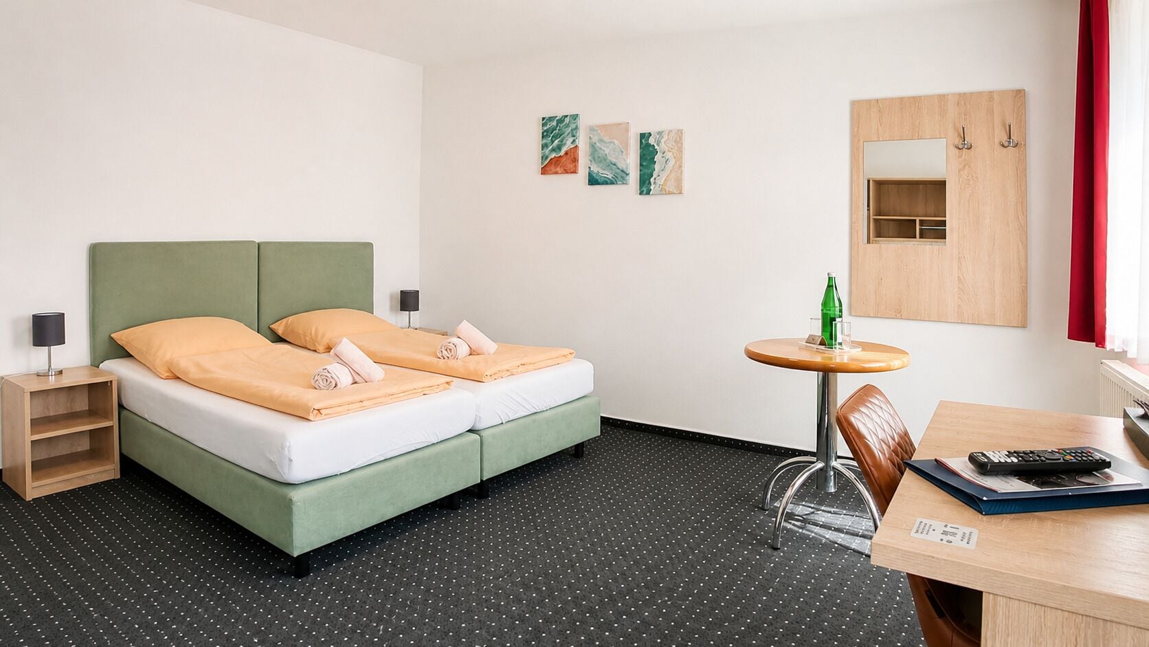 Habitación de hotel con cama, una mesita pequeña con una silla, una mesita de noche y un espejo.