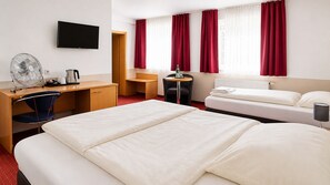 Habitación de hotel con cama, escritorio, silla, televisor y ventana con cortinas.