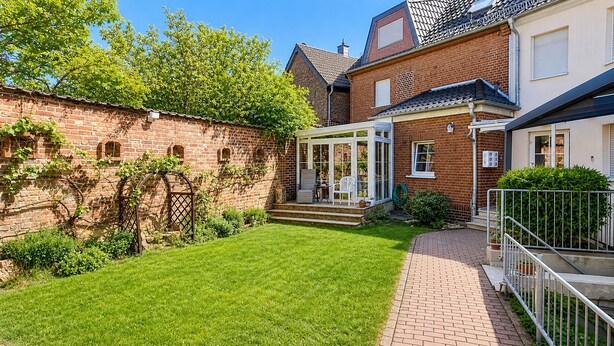 A brick house with a covered patio, a well-maintained lawn, and a brick pathway leading to the entrance. - Hotel am Weyerhof (Kerpen)