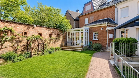 A brick house with a covered patio, a well-maintained lawn, and a brick pathway leading to the entrance.. Hotel am Weyerhof
