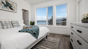 A bedroom with a large bed, a view of a lake, and a dresser with drawers. - Waterfront Home with
      Rooftop Hot Tub (West Kelowna)