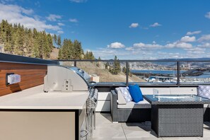An outdoor patio with a grill, seating area, and a view of a cityscape. - Waterfront Home with
      Rooftop Hot Tub (West Kelowna)
