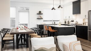 A modern kitchen with a central island, pendant lighting, and a dining area with a table set for four. - Waterfront Home with
      Rooftop Hot Tub (West Kelowna)