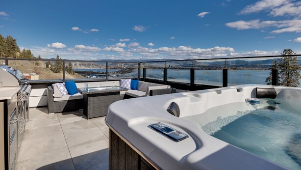 A rooftop patio with a hot tub, seating area, and a view of the cityscape. - Waterfront Home with
      Rooftop Hot Tub (West Kelowna)
