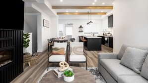 A modern living room with a fireplace, dining area, kitchen, and a grey sofa. - Waterfront Home with
      Rooftop Hot Tub (West Kelowna)
