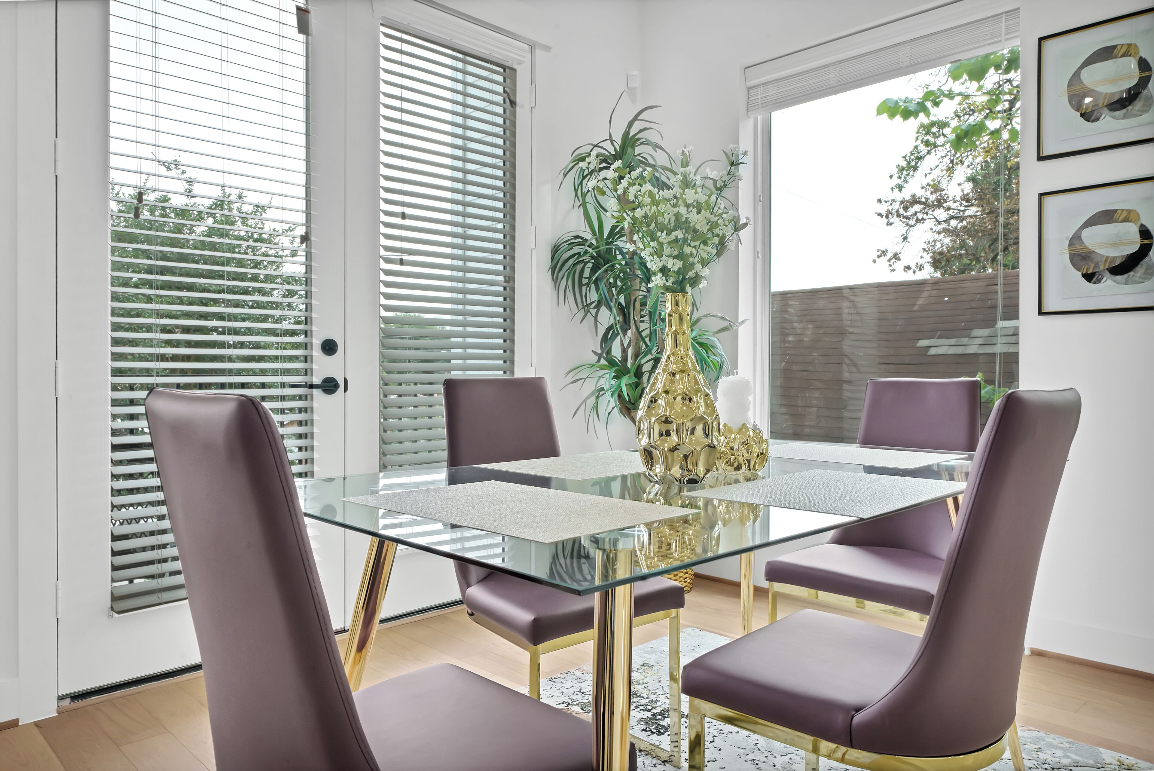 Un coin repas avec une table en verre, quatre chaises, un vase de fleurs et une vue par la fenêtre.