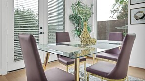 Un coin repas avec une table en verre, quatre chaises, un vase de fleurs et une vue par la fenêtre.