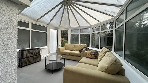 A conservatory with a glass ceiling, beige sofas, a glass coffee table, and a bookshelf. - Spacious 5BR Watford Home - Sleeps 10 - Parking (Watford)
