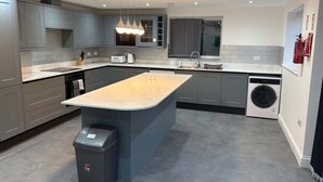 A modern kitchen with grey cabinetry, a central island, a built-in washing machine, and pendant lighting. - Spacious 5BR Watford Home - Sleeps 10 - Parking (Watford)