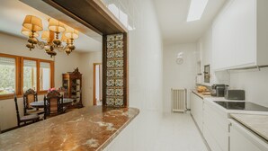 Ett kök med en bänkskiva i marmor, en kristallkrona, en pelare med målat glas och utsikt över utomhusmiljön genom ett fönster.