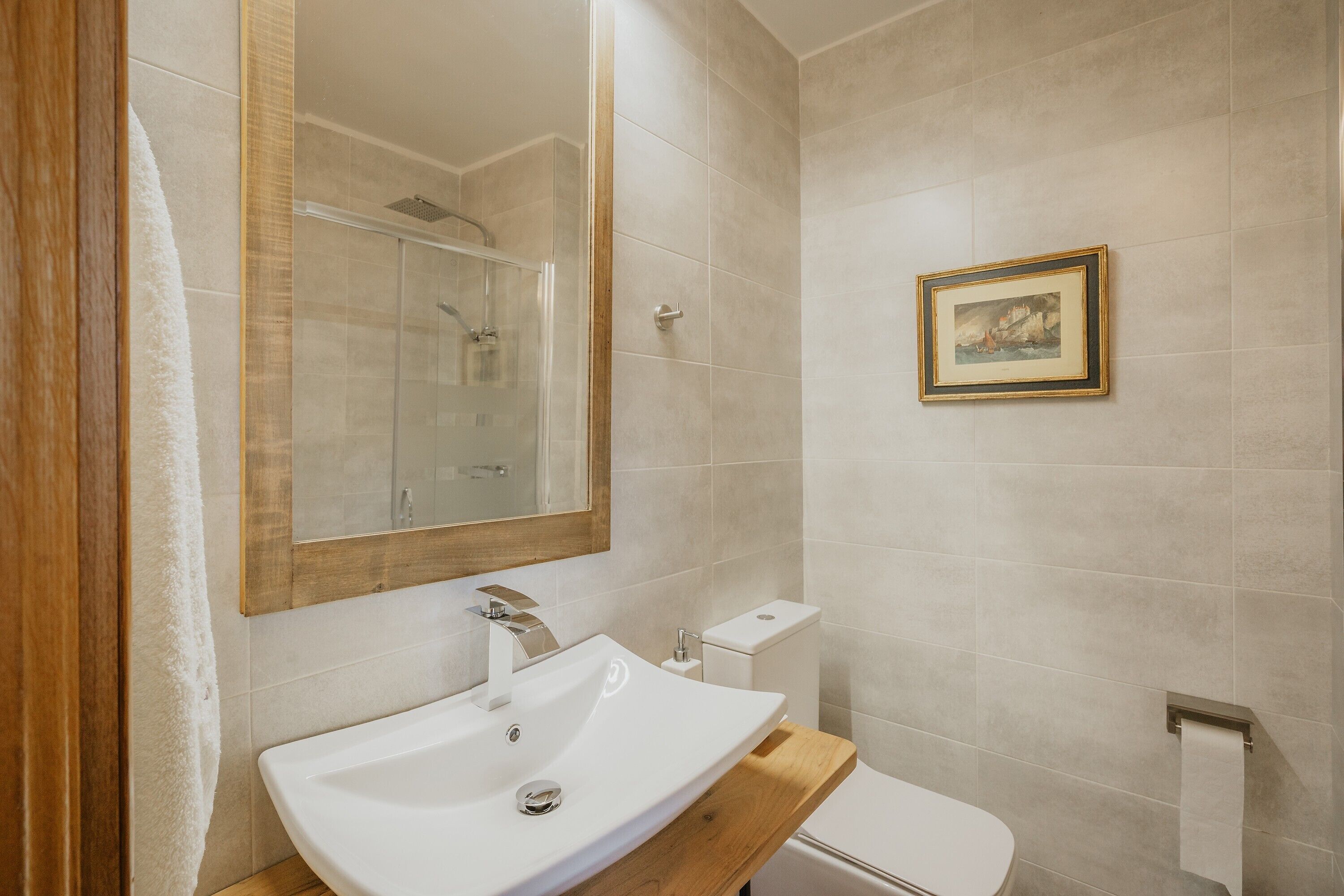 Un baño con un lavamanos blanco, un espejo, un inodoro y un cuadro enmarcado en la pared.