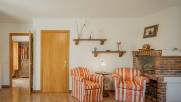 Een woonkamer met twee gestreepte fauteuils, een kleine tafel met een lamp, een open haard en een houten deur.