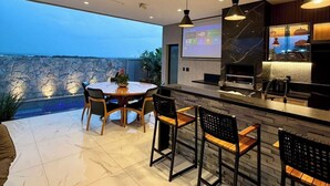 A modern kitchen with a large island, bar seating, and a dining area with a view of the sea. - Moto GP Goiânia - Casa Premium - Piscina (Senador Canedo)