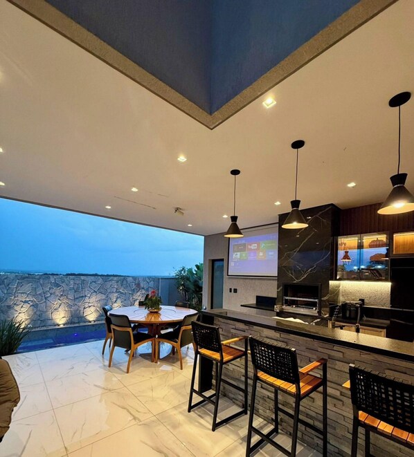 A modern kitchen with a large island, bar seating, and a dining area with a view of the sea. - Moto GP Goiânia - Casa Premium - Piscina (Senador Canedo)