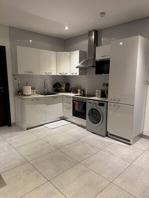 A modern kitchen with white cabinets, a built-in oven, a washing machine, and a microwave. - Must-see, luxurious 2-bed condo at Signature Apts (Accra)