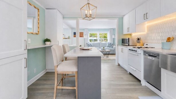 Een moderne keuken met witte kasten, een centraal eiland en een eetgedeelte met stoelen.