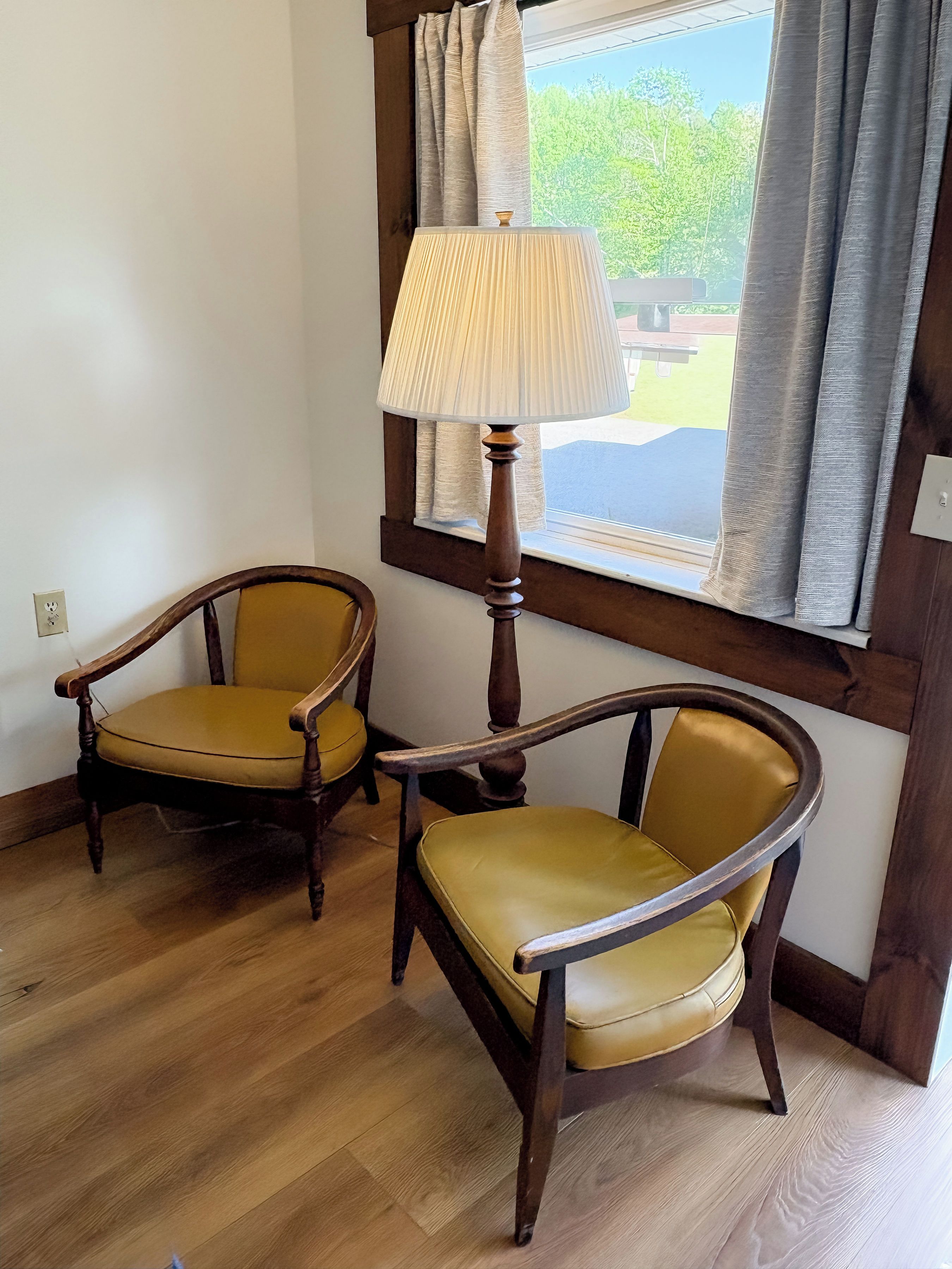 Two wooden chairs with yellow upholstery in a room with wooden flooring and a window with curtains.