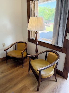 Deux chaises en bois recouvertes d’un tissu jaune, dans une pièce dont le sol est en bois et qui possède une fenêtre avec des rideaux.