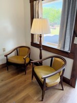 Dos sillas de madera con tapicería amarilla en una habitación con piso de madera y una ventana con cortinas.
