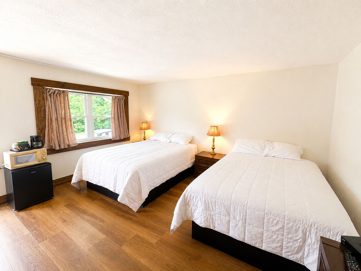 Een kamer met twee bedden, een klein tafeltje met een koffiezetapparaat en een raam met gordijnen.