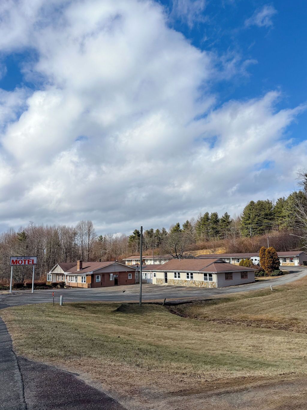 A motel with a signboard, a parking lot, and a hilly landscape in the background.