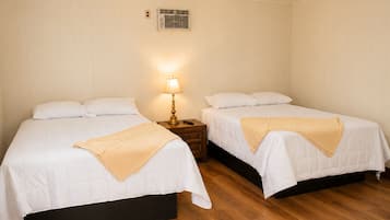 A hotel room with two beds, a bedside table with a lamp, and a wall-mounted air conditioning unit.