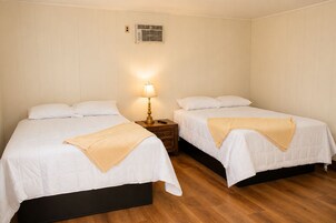Habitación de hotel con dos camas, una mesita de noche con lámpara y un aire acondicionado de pared.