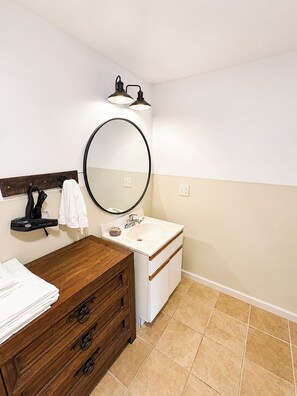 A bathroom with a wooden vanity, a round mirror, a sink, and a towel rack.