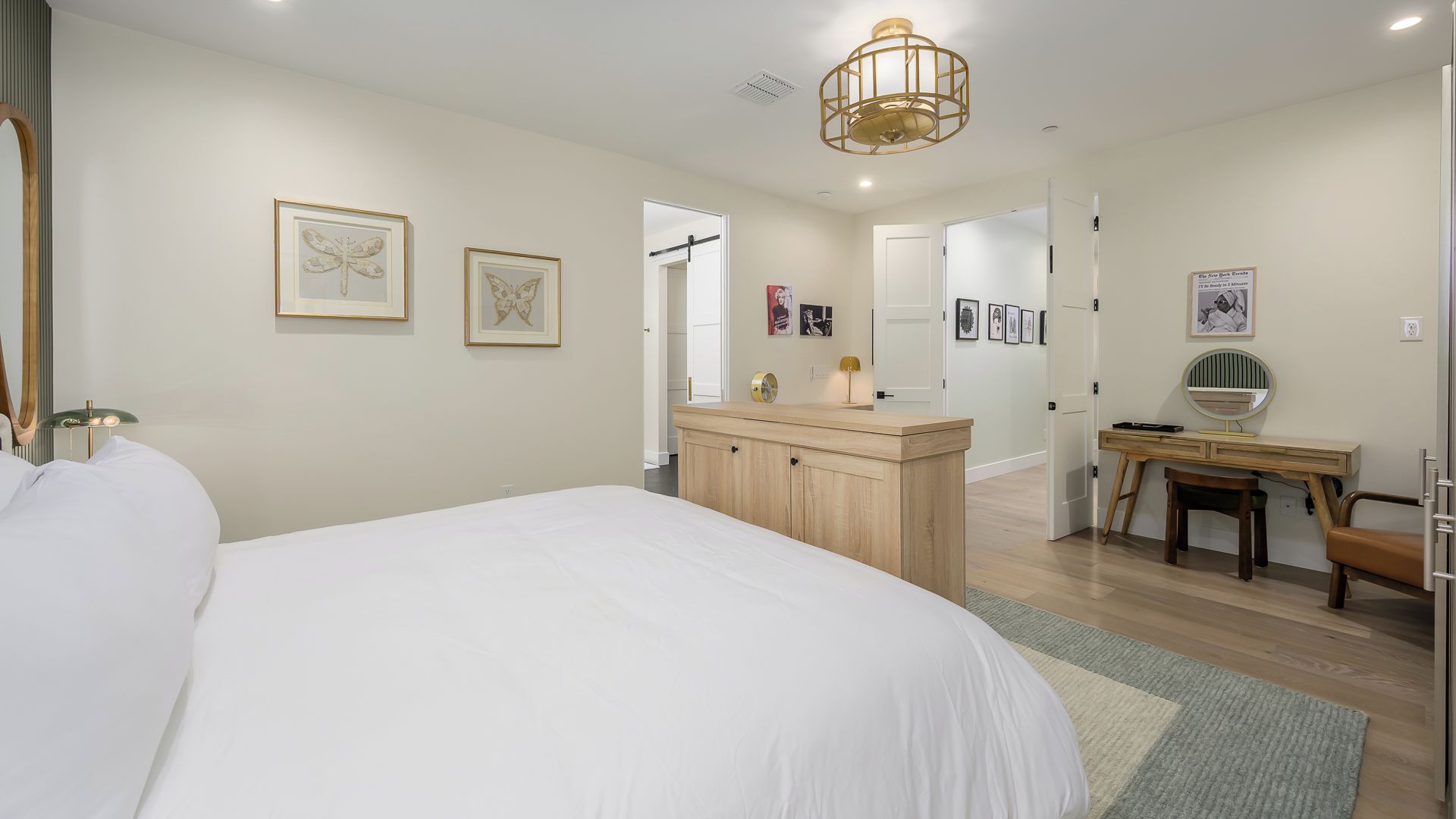 A bedroom with a large bed, a wooden dresser, a desk with a chair, and framed artwork on the walls.
