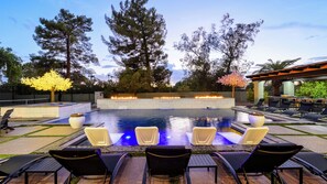 A swimming pool with a fire feature, surrounded by lounge chairs and trees. - Kierland Luxury 5BR Retreat w/ Pool, Spa, Golf Sim, Putting Green & Sport Court (Scottsdale)