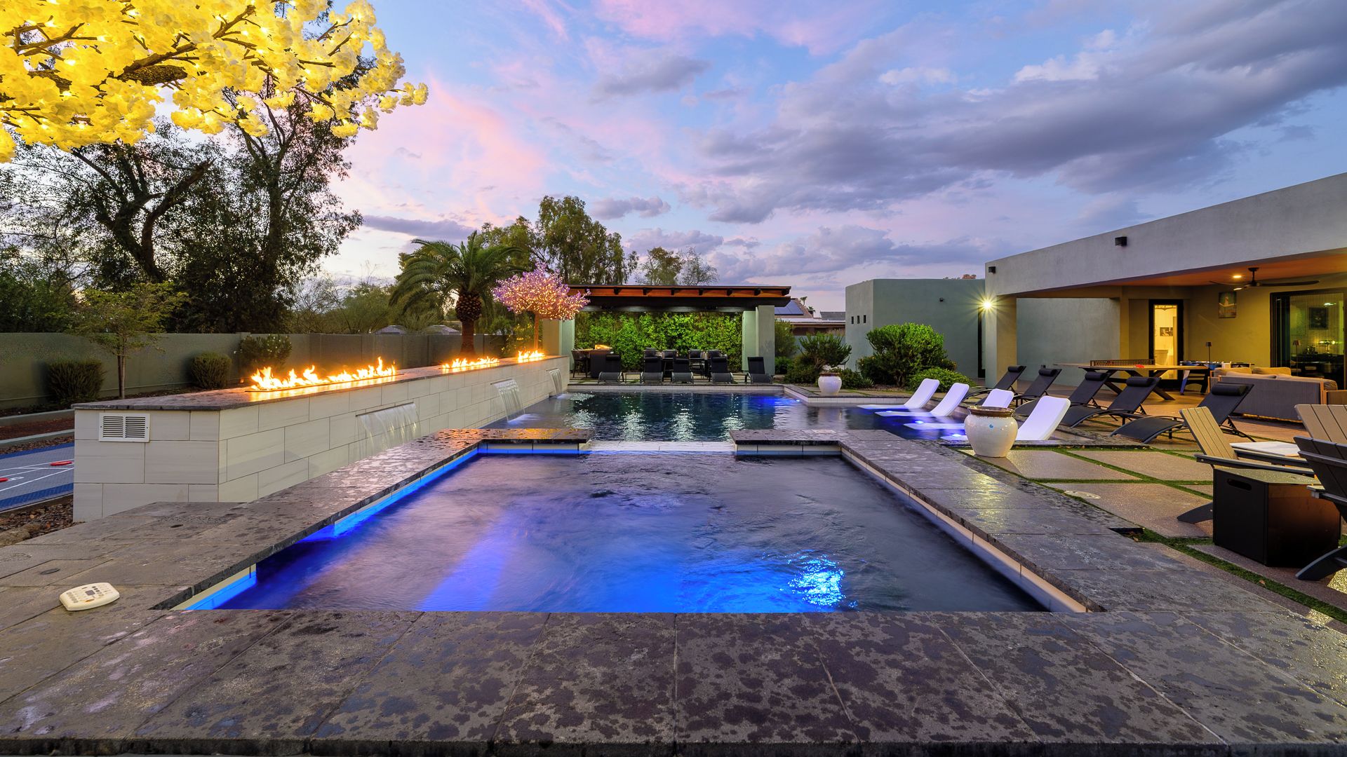 A swimming pool with a fire feature, lounge chairs, and a covered seating area.