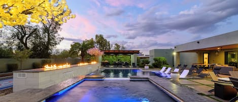 Una piscina con una chimenea, sillas de descanso y un área de estar techada.