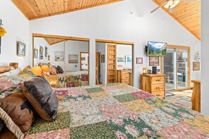 A bedroom with a large bed, wooden ceiling, a television, and a sliding glass door leading to a balcony.
