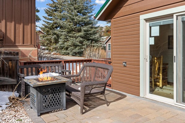 A patio with a fire pit, outdoor furniture, and a sliding glass door leading to a covered area.