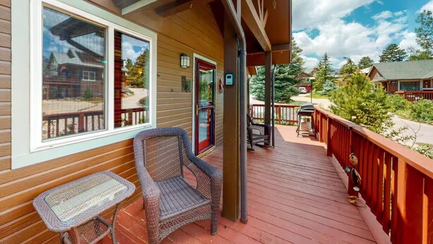 A wooden deck with outdoor seating, a covered area, and a view of surrounding buildings and trees.