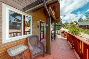 A wooden deck with outdoor seating, a covered area, and a view of surrounding buildings and trees.