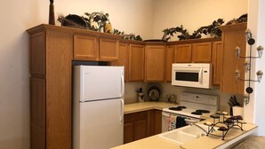 Una cucina compatta con mobili in legno, un frigorifero bianco, un forno a microonde e un piano cottura.
