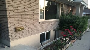 Um edifício residencial com fachada de tijolos, uma janela pequena e um canteiro de flores vermelhas.