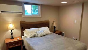 Quarto com cama, duas mesas de cabeceira com abajures, janela e ar condicionado.
