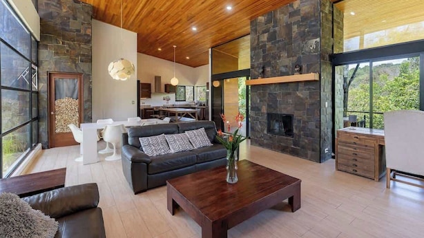 A modern living room with a fireplace, a dining area, and a kitchen visible through glass walls.