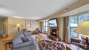 Een woonkamer met een open haard, een televisie en een groot raam.
