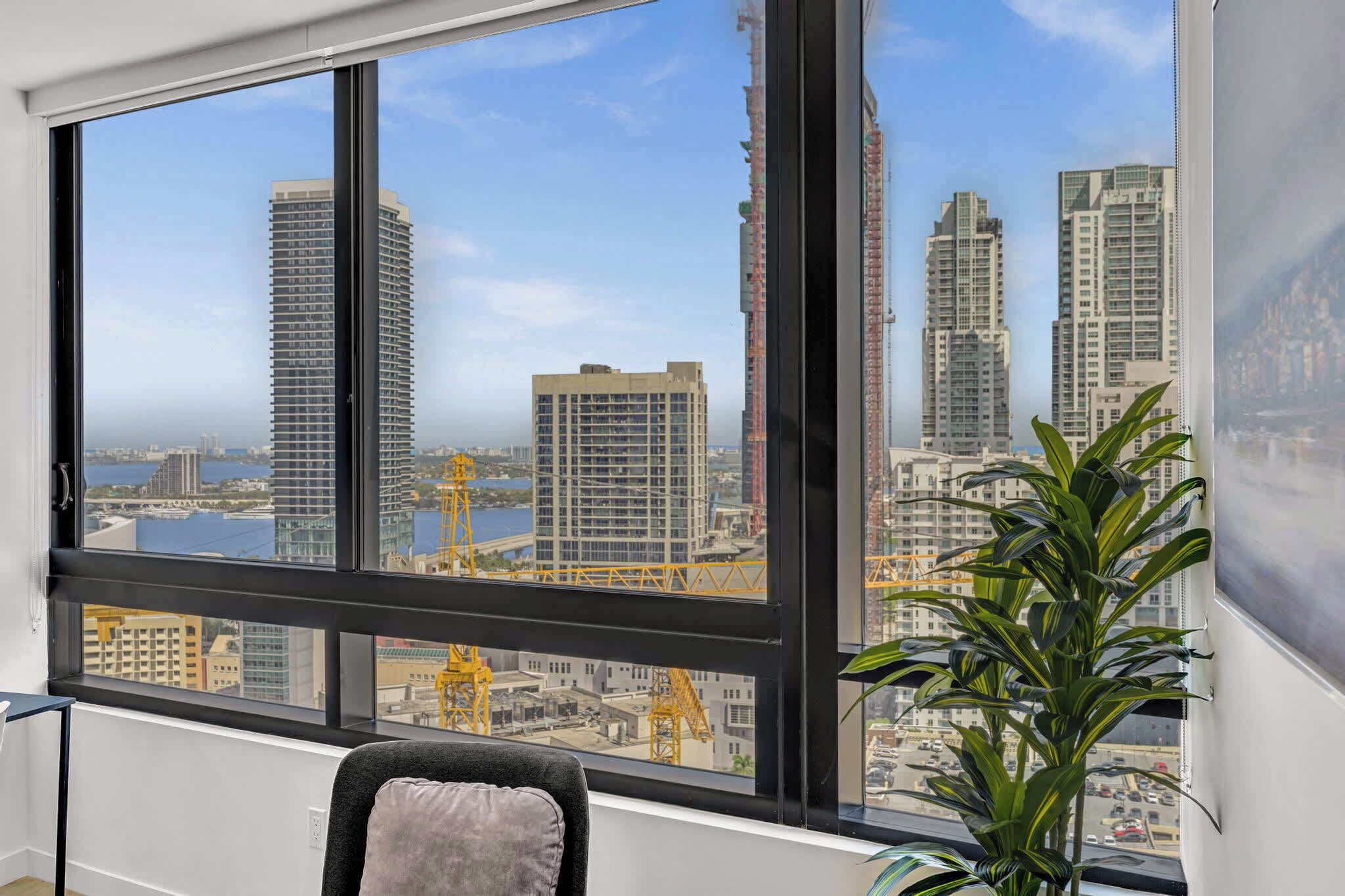 A room with a large window overlooking a cityscape with high-rise buildings and construction cranes.