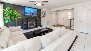 A modern living room with a fireplace, white sofas, a TV, and a ceiling fan.