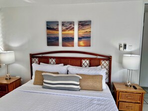 Ein ordentlich bezogenes Bett mit weißer Bettwäsche, einem Holz-Kopfteil und drei an der Wand befestigten Sonnenuntergangsbildern.