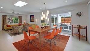 Een moderne woonkamer met een eethoek, met een grote houten tafel, oranje stoelen en een plafondlamp.