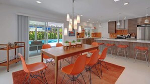 Een moderne keuken met een centraal eiland, een eethoek met oranje stoelen en een groot raam met uitzicht op een zwembad.