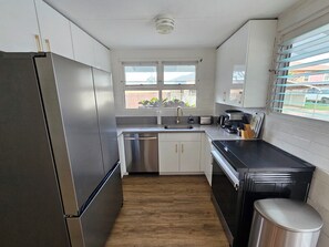 Eine moderne Küche mit Edelstahlgeräten, weißen Schränken, Holzboden und einem Fenster mit Jalousien.