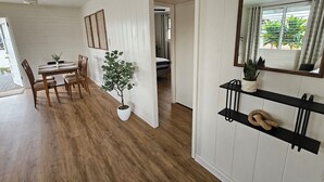 Una habitación con una mesa de comedor, sillas, una planta en maceta, un espejo y una estantería con una planta y un objeto decorativo.